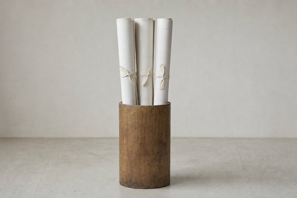 Three rolled sets of large plan sheets tied with cotton tape standing upright in a plain wooden tube.