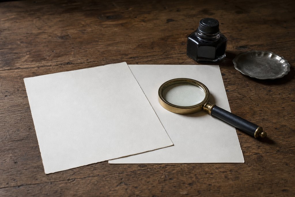 Two blank sheets of paper side by side on a wooden table, a brass-rimmed magnifying glass resting across one.