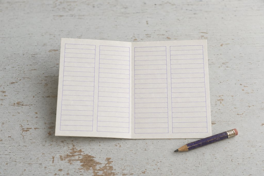 A folded card with four narrow blank ruled columns open on a wooden table, a pencil stub across one corner.