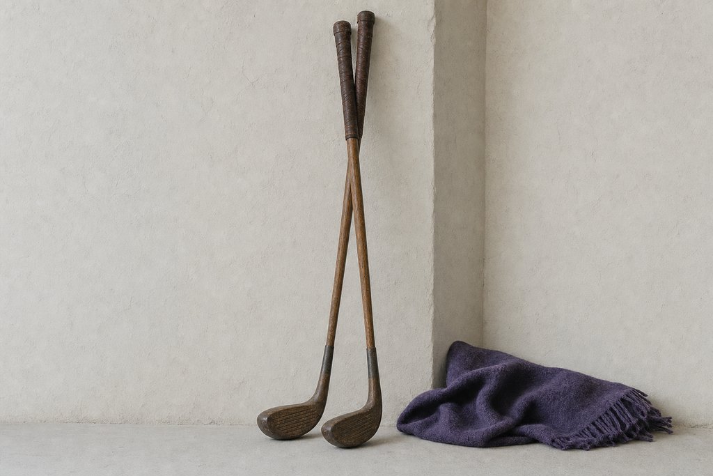 Two antique hickory-shafted golf clubs with plain unmarked heads leaning together in a plastered wall corner.
